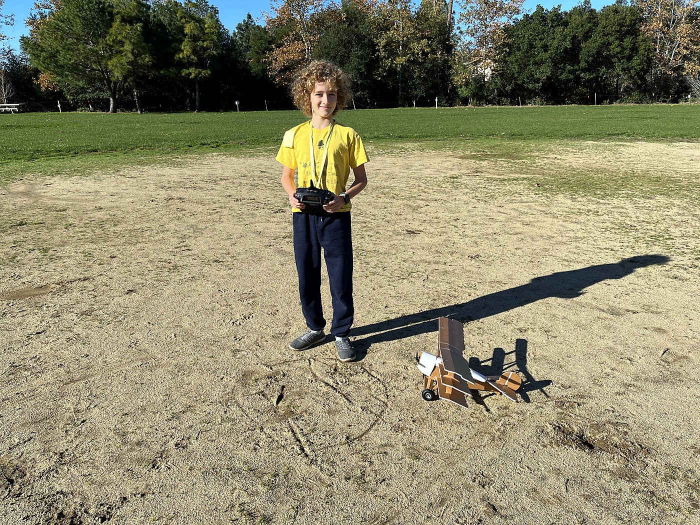 Standing on a dirt field with a transmitter, the FT DR1 triplane on the ground