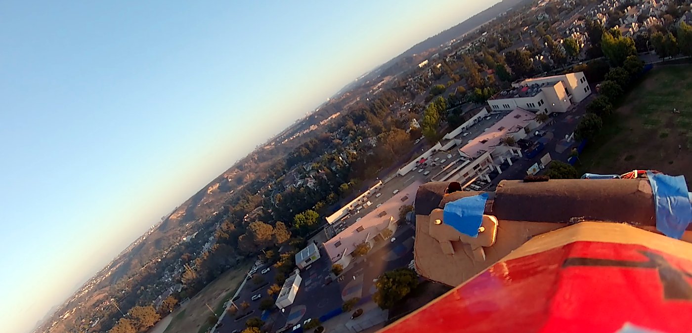 FPV view from the Simple Scout over a neighbourhood, its red wing in frame