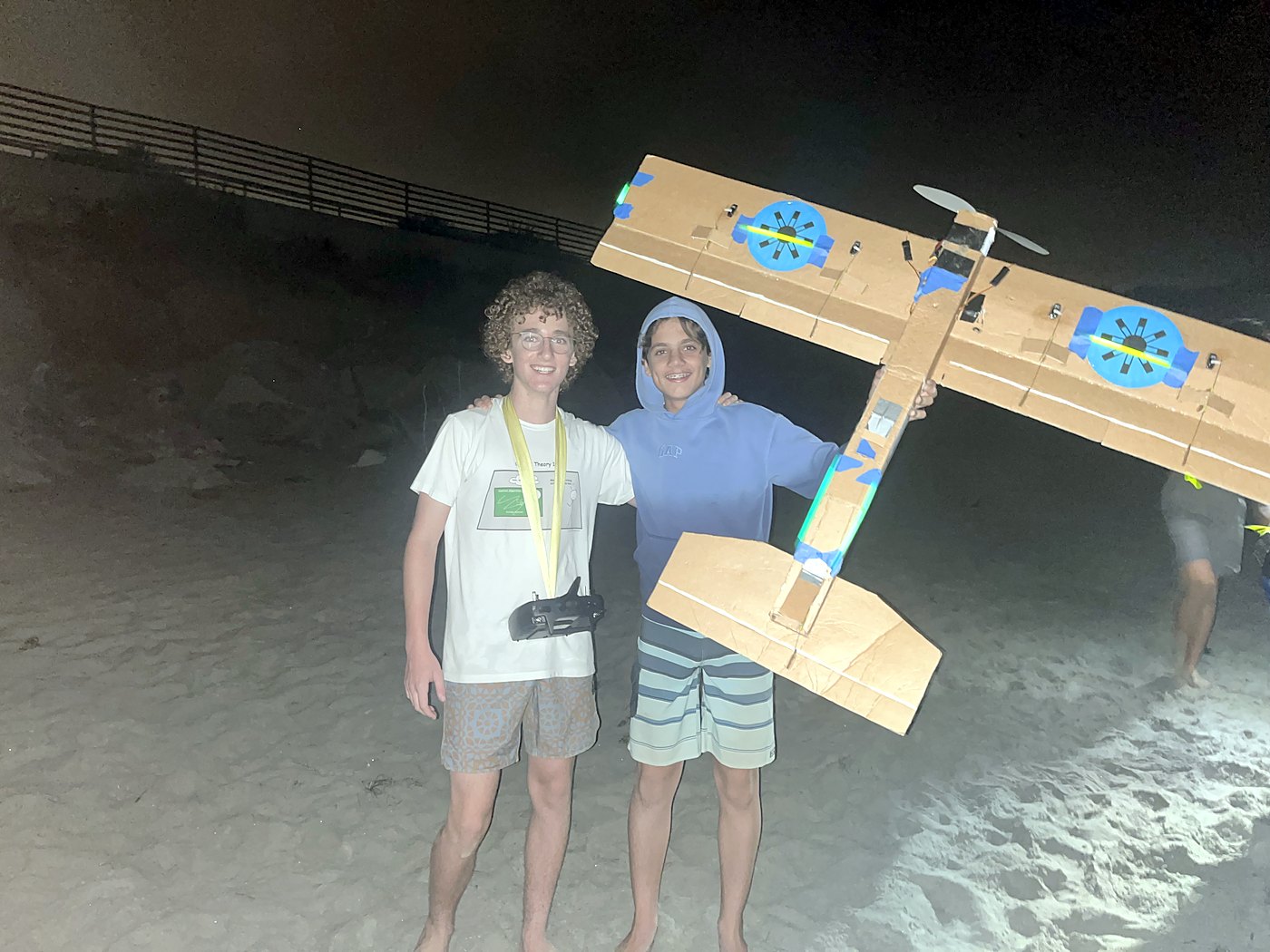 Two teenagers on a beach at night holding up Mother Hen